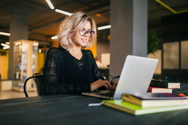portrait-young-pretty-smiling-woman-sitting-table-black-shirt-working-laptop-co-working-office-wearing-glasses_285396-79